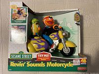 Sesame Street Ernie and Bert Revin' Sounds Motorcycle toy in original box, front view showing characters and branding.