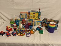 Photo shows assortment of vintage kids toys including four character toy cars, multiple colorful candy dispensers, rainbow rubber bracelets, sidewalk chalk, stack of colorful plastic cups, small toys and figurines.