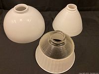 Three glass lamp shades grouped on a black surface: one solid white, one white waffle pattern conical, one clear and white waffle pattern diffuser.