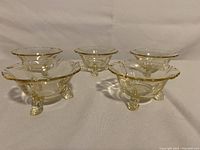 Five yellow tinted glass nut dishes with dolphin-shaped feet on a white surface, viewed at an angle