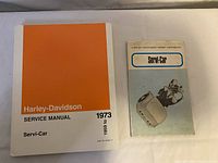 Two Harley-Davidson Servi-Car manuals side by side: 1973 Service Manual on left and Rider Handbook on right.