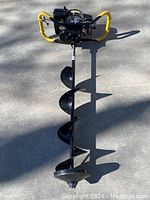 Full view of the Cobra ice auger showing the yellow handles, spiral drill blade, and engine mount on concrete surface.