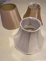 Three lamp shades placed on a surface showing the white scalloped edge shade and two brown tones.