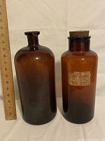 Photo showing both large brown glass bottles side by side with ruler for scale.