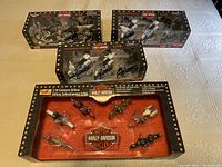 Photo showing 4 boxed sets of Harley Davidson model motorcycles. A large box contains 8 mini motorcycles. Three smaller boxes contain 3 motorcycles each in white and black colors.