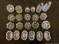Top view of all 20 glass pieces arranged on black background, showing open salt cellars and glass shakers with metal tops.