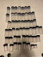 Full set of 43 clear plastic jars with black lids arranged on a surface, showing different sizes.