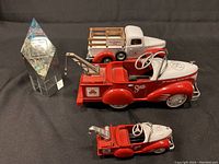 Photo showing all four items: two red and white State Farm diecast tow trucks (large and small), a white and red Car Finance Plan diecast truck with wooden flatbed, and a clear pyramid-shaped FLMI glass paperweight with etched text.