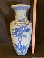 Full view of the tall blue and white porcelain vase with ruler to show height near 21 inches