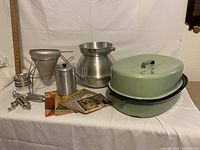Photo of vintage kitchen items including aluminum cone sieve strainer with stand, Vita Craft aluminum bowl with cone strainer, metal coffee canister, and green enamel roaster with lid on white background.