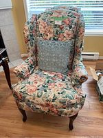 Single floral print armchair shown with blue-gray decorative pillow and wooden legs under natural light.