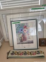 Multiple framed floral paintings stacked against the wall including one by Julia Rowntree with flowers in vases.