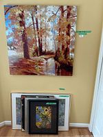 Group of 5 framed paintings leaning against wall including floral, abstract styles and one empty frame.