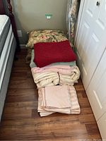 Photo of entire bedding lot stacked on the floor showing blankets, sheets, and floral pillows