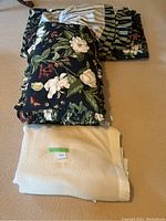 Floral bedding folded with beige bath towel on top on carpeted floor