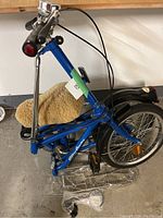 Blue fold-up bicycle folded with visible frame, padded seat, and pedals taken from side angle.