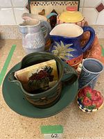 Photo showing ceramic jugs, bowl with handle, tile, rooster and vase on a kitchen counter