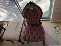Photo of Victorian style pink tufted upholstered chair with carved wooden frame and matching footstool in front.