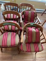 Six wooden chairs with striped cushions grouped together on wooden floor. Two chairs with arms, four armless. Each cushion features vertical stripes in red, beige, and cream colors. Cushions include seats and back pillows.