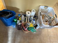 Photo showing assortment of cleaning supplies including bottles of cleaning liquids, paper towels, laundry basket with hangers, step stool, and reusable bag with more items.