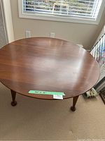 Full view of the low round wooden coffee table sitting on a carpeted floor near a window, showing the tabletop and legs.