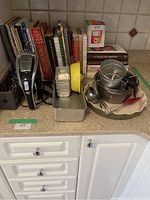 Overall view of lot showing cookbooks, mixing bowls, baking pans, measuring cups, mixer, and other accessories on kitchen counter.