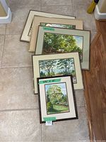 Five framed landscape paintings arranged on the floor showing varying sizes with a floor tile background