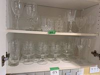 Top and middle shelf showing various styles of glassware with stems including goblets and wine glasses