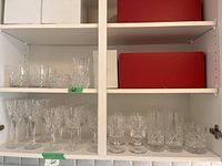 Shelf displaying various clear crystal glassware including wine glasses, highball glasses, a bowl, and a vase, alongside several white and red empty packing boxes.