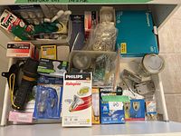 Drawer with assorted household items including light bulbs, flashlight, gloves, and nails, mostly in original packaging.