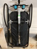 Front view of inversion table folded with visible padded backrest and ankle support rollers, black metal frame.