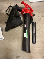Full view of red Homelite electric leaf blower vac with black collection bag and detachable black nozzle on concrete floor