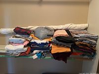 Stack of assorted fabric pieces in different colors, patterns, and textures with a long rolled white fabric behind