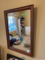 Mirror leaning against a wall reflecting a room interior with shelving and household items.