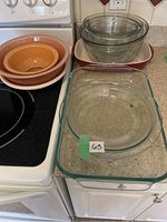 Photo showing stacked peach and beige ceramic bowls or pie plates, clear glass mixing bowls, and a rectangular glass casserole dish on kitchen counter.