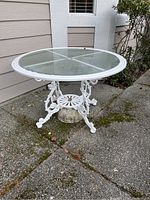 Front view of assembled white cast iron table with round glass top, showing decorative base.