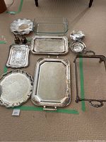 Photo of assorted metal serving trays, candy bowl, bells, clear glass casserole dish, and metal casserole dish holder on carpeted floor