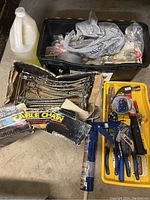 Photo showing black tool box filled with assorted hand tools, a container of liquid, and box of car cable chains with loose chains on floor