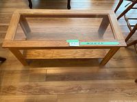 Top view of rectangular wooden coffee table showing clear glass insert, wooden frame, and lower shelf on wooden floor.