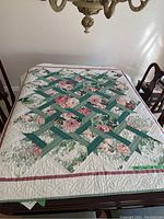 Full view of patchwork quilt tablecloth on dining table showing floral and lattice geometric pattern with pink border edges.