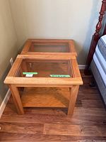 Pair of wooden side tables with glass inset tops and wooden lower shelves, showing overall condition and design.