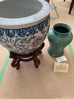 Photo of green crackled ceramic vase on wooden stand and adjacent large ceramic planter on carpet.
