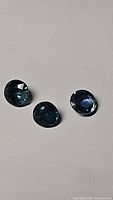 Three natural blue round cut sapphires placed on a light surface showing color and clarity.