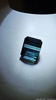 Close-up of the rectangular emerald cut blue Paraiba tourmaline under direct light highlighting its clarity and color.