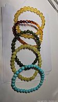 Photo of six elastic beaded bracelets arranged in overlapping circles showing colors and bead shapes.