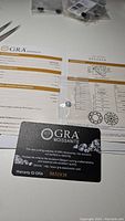 Close-up of GRA certification report and card for the moissanite stone with grading details and laser inscription, displays authenticity and grading information.