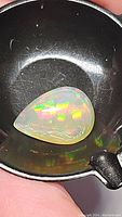 Close-up photo of pear-shaped Ethiopian opal showing vibrant multicolor play-of-color in a black dish.
