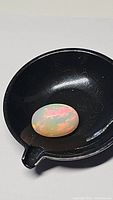 Oval-shaped, polished fire opal displaying multicolor flashes with a smooth cabochon finish, placed in a black container for display.