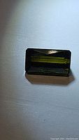 Front view of rectangular scissor cut green tourmaline gemstone on white background.