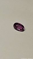 Close-up image showing the oval cut deep electric purple natural tourmaline gemstone on a plain light background.